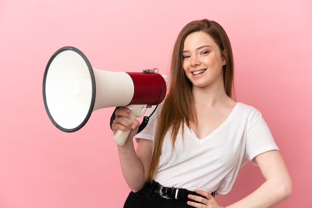 Fille adolescente sur fond rose isolé tenant un mégaphone et souriant