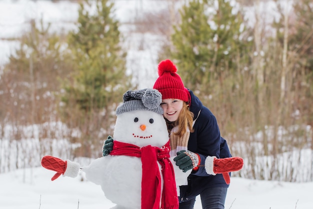 Fille adolescente heureuse avec bonhomme de neige dans la forêt d'hiver