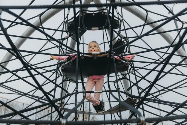 Photo fille adolescente heureuse jouant dans une toile d'araignée de corde à l'aire de jeux. sports pour enfants.