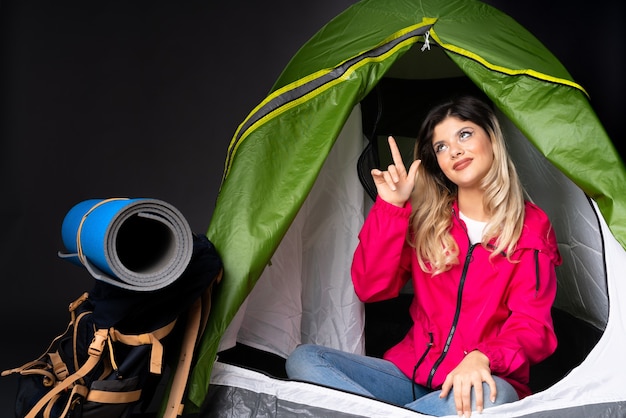 Fille adolescente à l'intérieur d'une tente de camping vert isolé sur fond noir pointant vers l'extérieur
