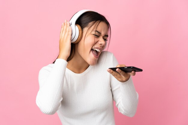 Fille adolescente isolée sur bleu écoute de la musique avec un mobile et le chant