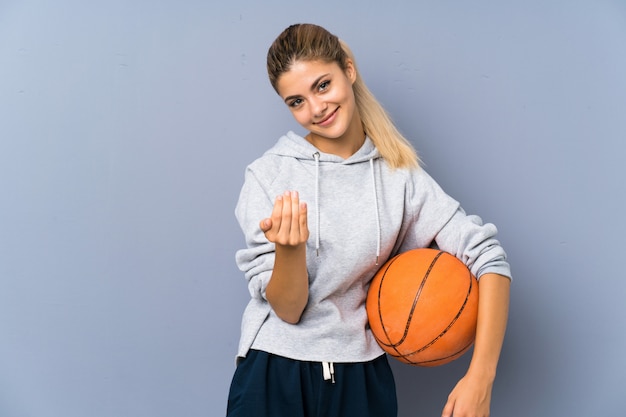 Fille adolescente jouant au basketball sur un mur gris invitant à venir avec la main. Heureux que tu sois venu