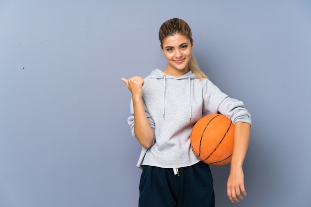 Photo fille adolescente jouant au basketball sur un mur gris pointant sur le côté pour présenter un produit