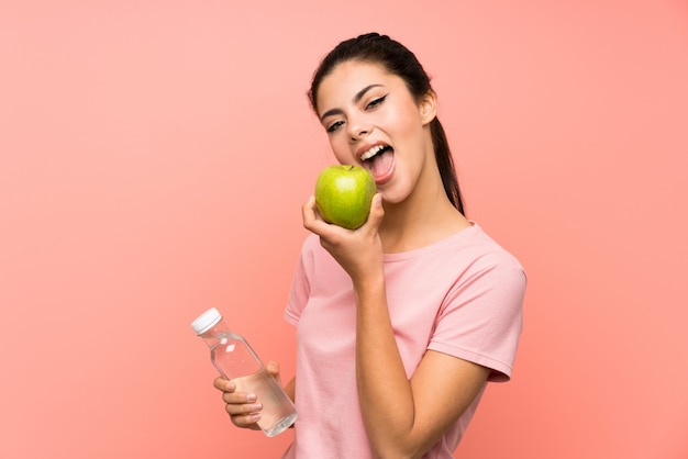 Fille adolescente sur mur rose isolé avec une bouteille d'eau et une pomme