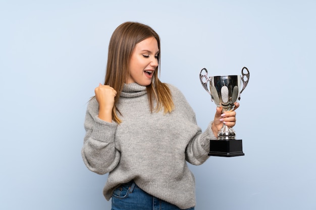 Fille adolescente avec pull sur mur bleu isolé, tenant un trophée