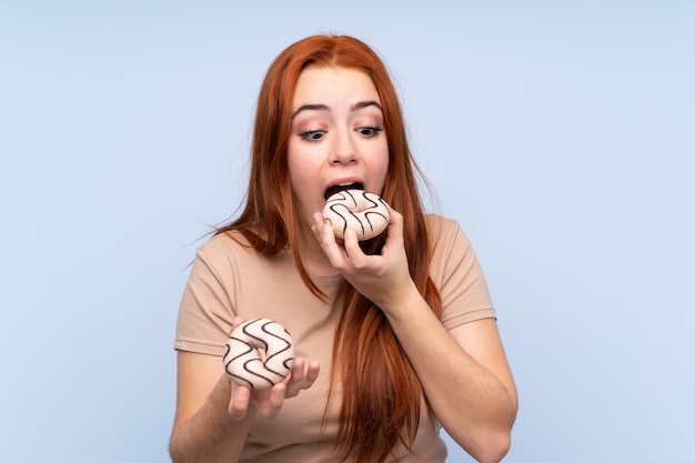 Fille adolescente rousse sur bleu manger un beignet