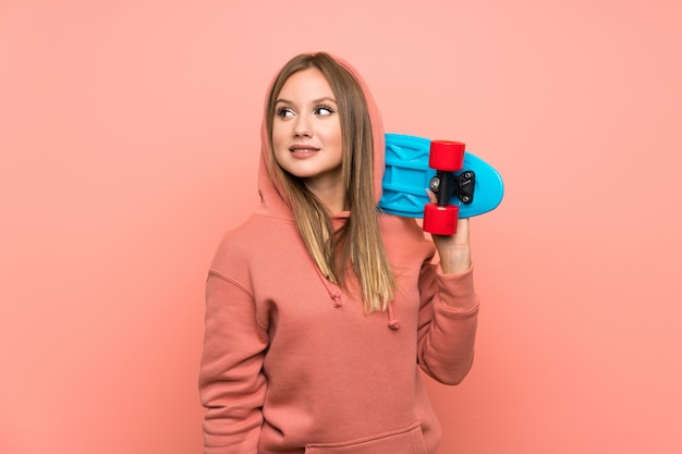 Fille adolescente avec skate sur mur rose isolé