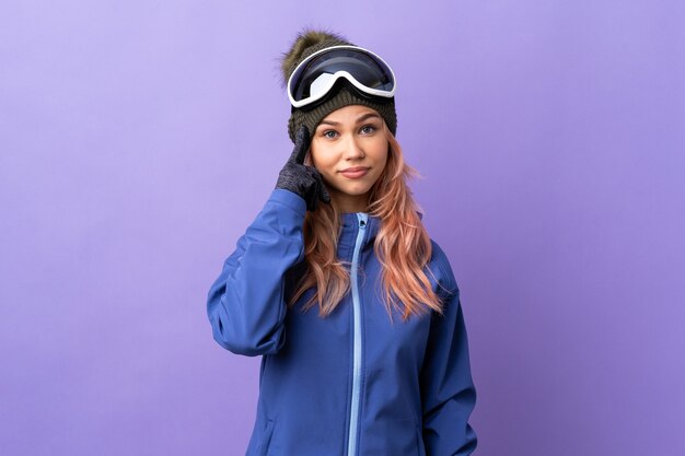 Fille adolescente skieur avec des lunettes de snowboard sur violet isolé pensant une idée