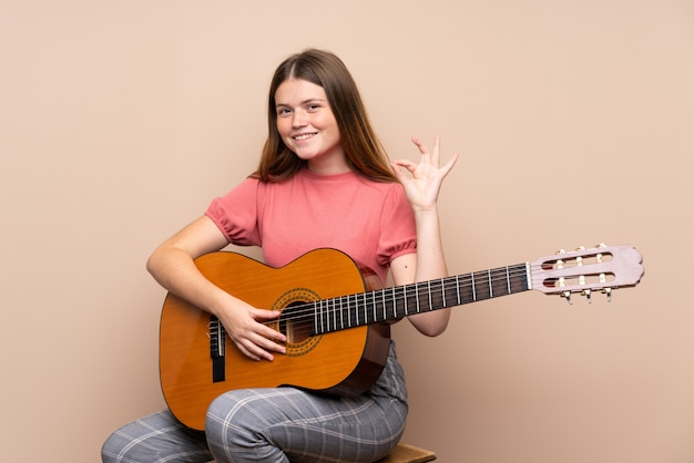 Fille adolescente ukrainienne avec guitare sur isolé montrant signe ok avec les doigts