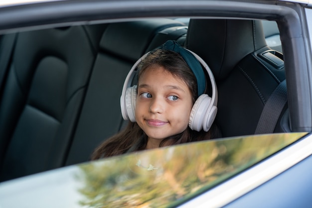 Fille adorable dans des écouteurs regardant par la fenêtre de voiture