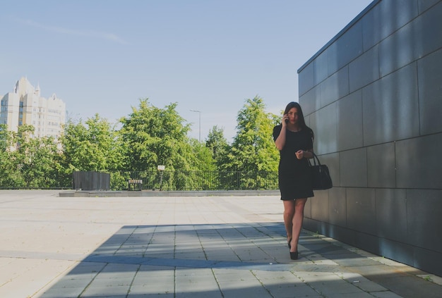 Fille d'affaires en robe noire près du mur parlant au téléphone