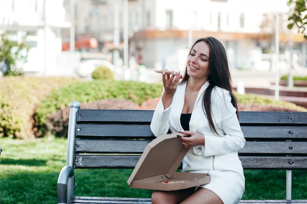 Fille d'affaires souriante, manger de la pizza dans la rue