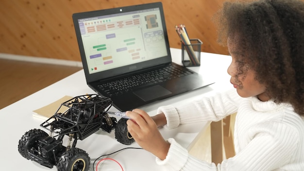 Photo une fille africaine construit une voiture robotique en utilisant des fils en utilisant un ordinateur portable