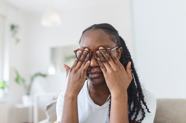 Une fille africaine à lunettes se frotte les yeux, souffrant d'yeux fatigués, concept de maladies oculaires