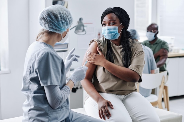 Fille africaine en masque consultant une infirmière après avoir été vaccinée lors de sa visite à l'hôpital