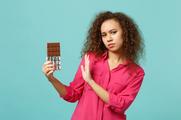 Fille africaine mécontente dans des vêtements décontractés montrant un geste d'arrêt avec paume à barre de chocolat isolée sur fond de mur bleu turquoise. Les gens émotions sincères, concept de style de vie. Maquette de l'espace de copie.