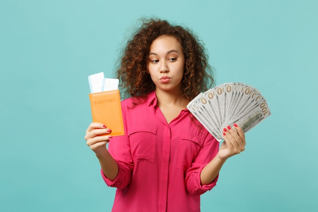 Une fille africaine perplexe tient un billet d'embarquement pour passeport, fan d'argent en billets de banque en dollars, de l'argent en espèces isolé sur fond bleu turquoise. Concept de mode de vie d'émotion sincère de personnes. Maquette de l'espace de copie.