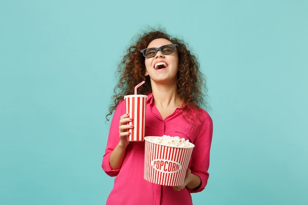 Fille africaine riante dans des lunettes imax 3d regardant un film de film tenir une tasse de pop-corn de soda isolé sur fond bleu turquoise en studio. Émotions des gens au cinéma, concept de style de vie. Maquette de l'espace de copie.