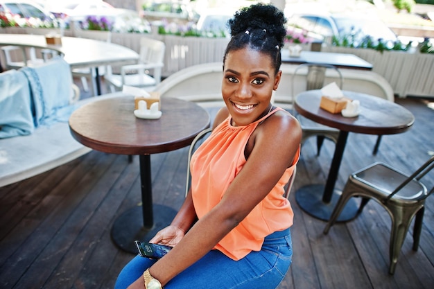 Fille afro-américaine assise sur une table de café avec téléphone portable