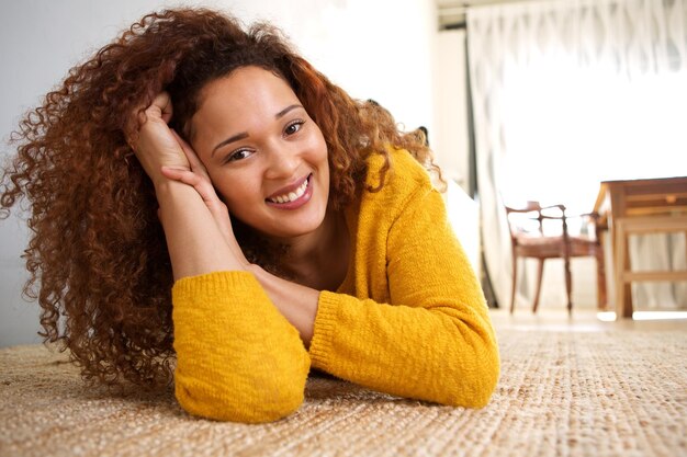 Une fille afro-américaine aux cheveux bouclés allongée sur le sol à la maison.