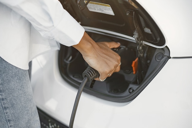 Fille afro-américaine chargeant une voiture électrique à la station-service électrique