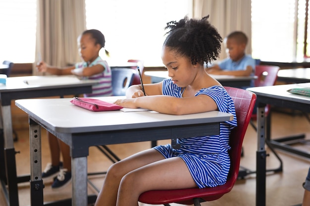 Fille afro-américaine étudiant assis sur son bureau dans la classe à l'école
