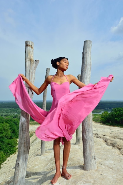 Une fille afro-américaine heureuse dans une robe rose au sommet d'une colline contre un beau paysage