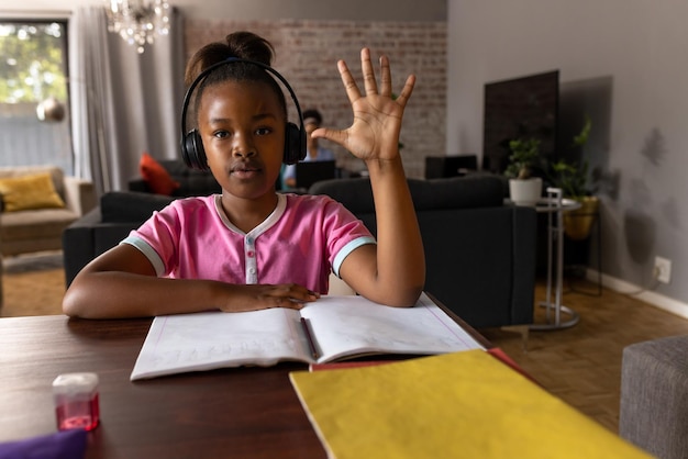 Une fille afro-américaine heureuse portant des écouteurs tenant la main pendant une leçon en ligne à la maison