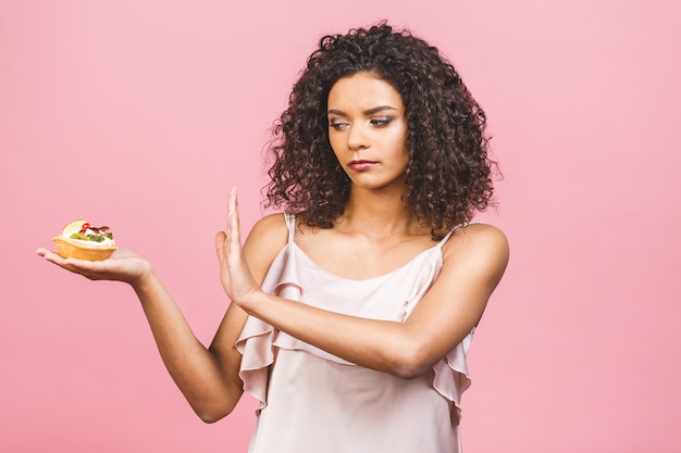 Une fille afro américaine ne mange pas de gâteau. Conception pour perdre du poids. Main faisant signe non à un gâteau. Isolé sur fond rose.