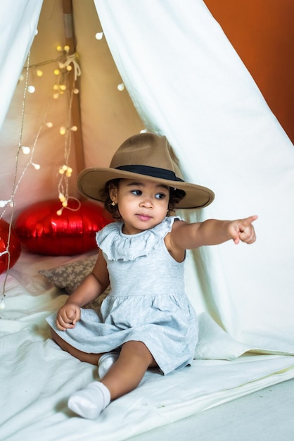 Fille afro-américaine noire jouer dans une tente wigwam enfant dans un chapeau montrant un doigt enfance heureuse