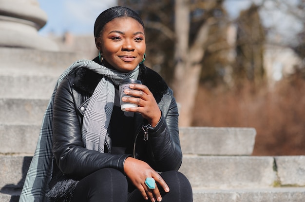 Fille afro-américaine se promène dans la place avec du café