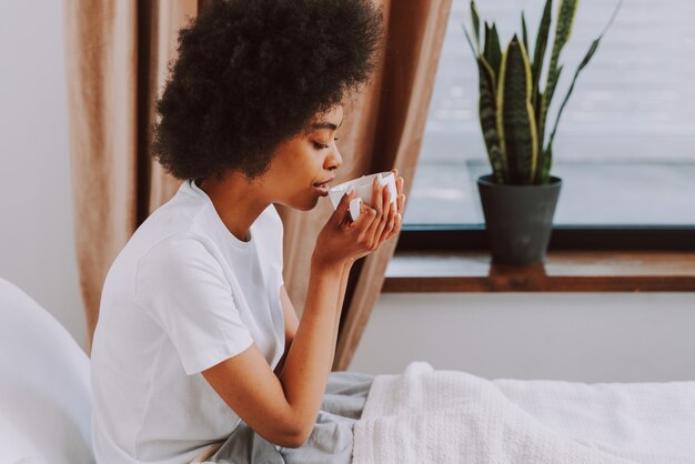 Fille afro-américaine se reposant dans son lit à la maison Belle femme se relaxant à la maison prenant son petit déjeuner au lit