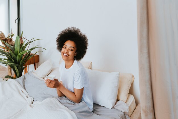 Fille afro-américaine se reposant dans son lit à la maison Belle femme se relaxant à la maison prenant son petit déjeuner au lit