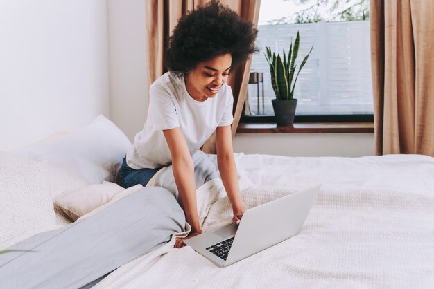 Fille afro-américaine se reposant dans son lit à la maison Belle femme se relaxant à la maison et utilisant un ordinateur portable