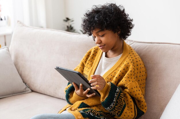 Fille afro-américaine tenant une tablette numérique à écran tactile tapant la page de défilement à la maison femme avec mobi