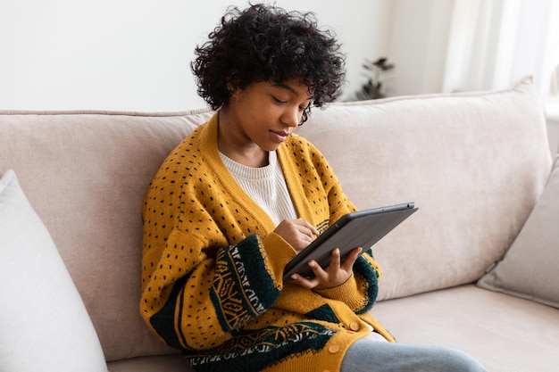 Fille afro-américaine tenant une tablette numérique à écran tactile tapant la page de défilement à la maison femme avec mobi