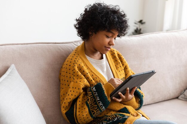 Fille afro-américaine tenant une tablette numérique à écran tactile tapant la page de défilement à la maison femme avec mobi