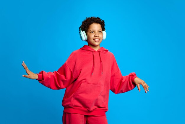 Photo une fille afro-américaine en vêtements décontractés écoutant de la musique dans des écouteurs et dansant contre le bleu