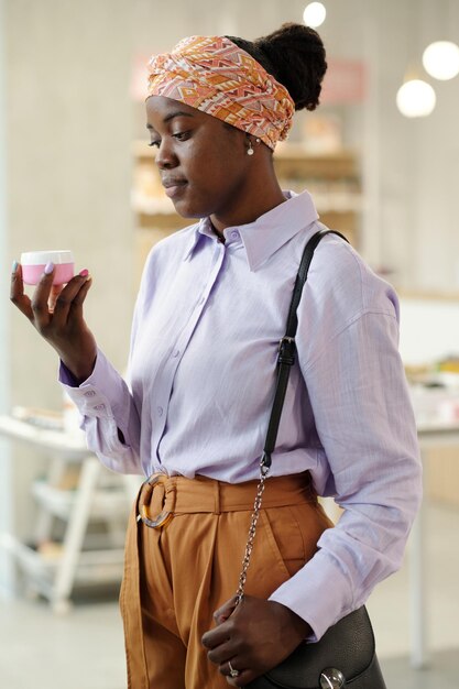 Fille afro-américaine en vêtements décontractés intelligents choisissant une crème hydratante pour le visage