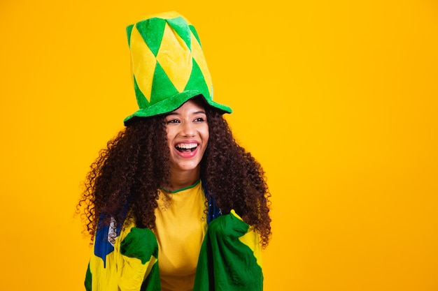 Fille afro encourageant l'équipe brésilienne préférée, tenant le drapeau national sur fond jaune.