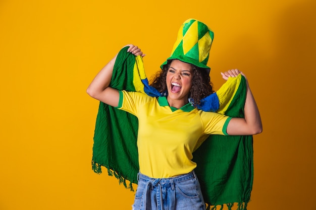 Fille afro encourageant l'équipe brésilienne préférée, tenant le drapeau national sur fond jaune.