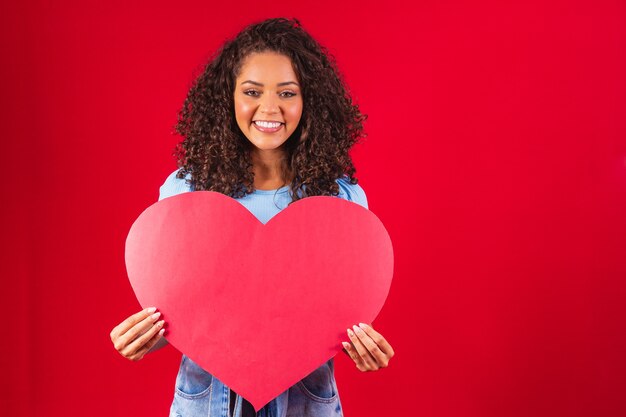 Fille afro tenant dans les mains amour en forme de coeur isolé sur fond rouge