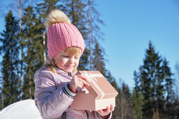 Fille d'âge préscolaire avec boîte-cadeau brillante à l'extérieur de la journée d'hiver par temps ensoleillé et froid