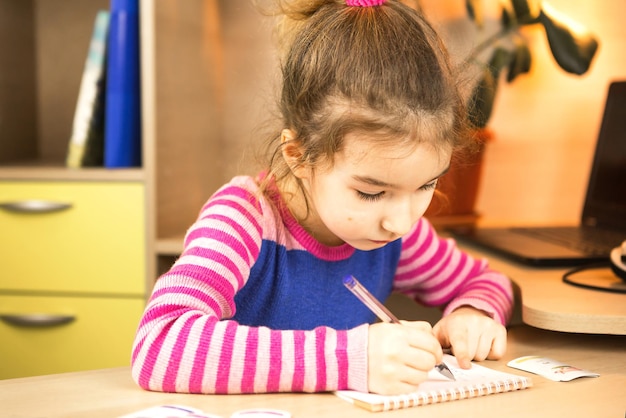 Une fille d'âge préscolaire est engagée à la maison à la table à étudier une écriture de programme éducatif