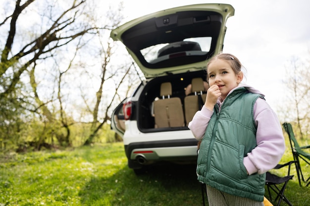 Fille d'âge préscolaire en gilet sans manches vert contre le coffre ouvert de la voiture en pique-nique