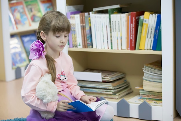 Une fille d'âge préscolaire lit un livre L'enfant est à la bibliothèque Lire des livres