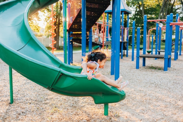 Une fille d'âge préscolaire de race mixte s'amuse à l'extérieur pendant l'été dans un parc de jeux.
