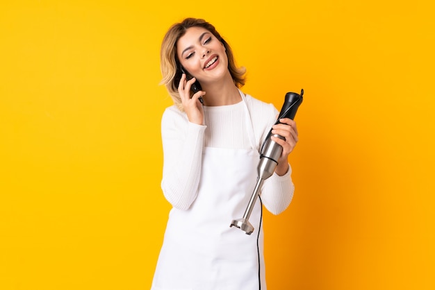 Fille à l'aide d'un mixeur plongeant en gardant une conversation avec le téléphone mobile avec quelqu'un