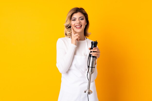 Fille à l'aide d'un mixeur plongeant souriant avec une expression heureuse et agréable