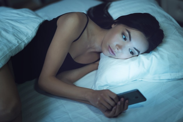 Fille à l&#39;aide de smartphone sur le lit avant de dormir